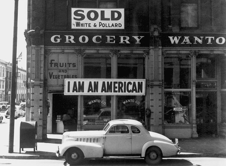 A Japanese American unfurled this banner the day after the Pearl Harbor attack. Dorothea Lange photographed it in March 1942, just prior to the man's internment. Wikimedia Commons.